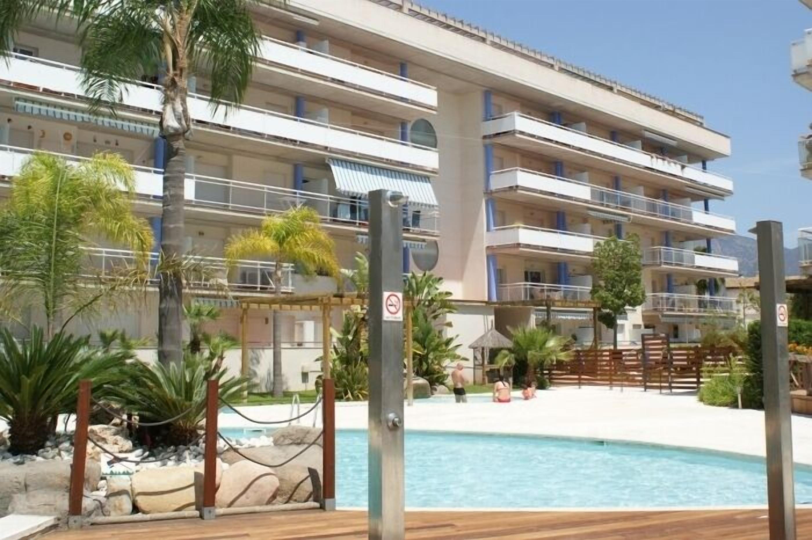 Ein mehrstöckiges Hotel mit Balkonen, einem Swimmingpool und tropischer Bepflanzung.