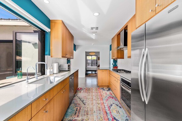 A modern kitchen with wooden cabinets, stainless steel appliances, and a colorful rug.