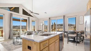 A modern kitchen with a large island, a dining area with a table and chairs, and large windows offering views of the outdoors. - Elk View-Access Elk River-Rural Acreage-Huge Patio (Noel)