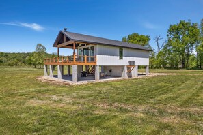 A single-story house with a covered porch, a small deck, and a large open lawn area.