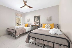 A bedroom with two beds, a ceiling fan, a window with blinds, and wall decor.