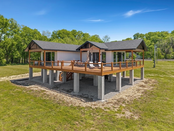 A two-story wooden structure with a deck, large windows, and a covered outdoor seating area.