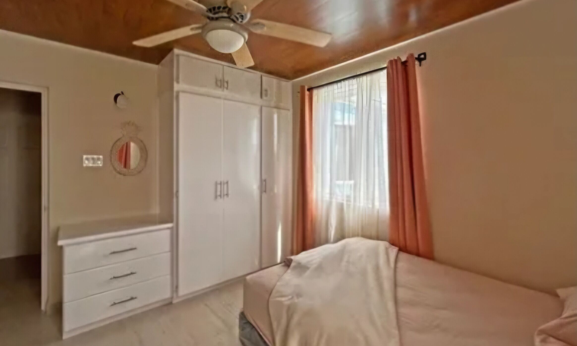 Een slaapkamer met een bed, een kledingkast, een plafondventilator en een raam met gordijnen.