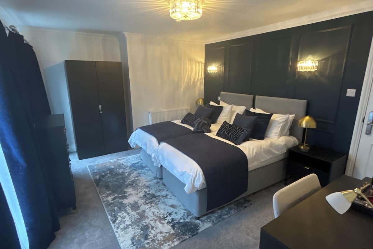 A modern bedroom with a large bed, bedside lamps, a desk, and a wardrobe.