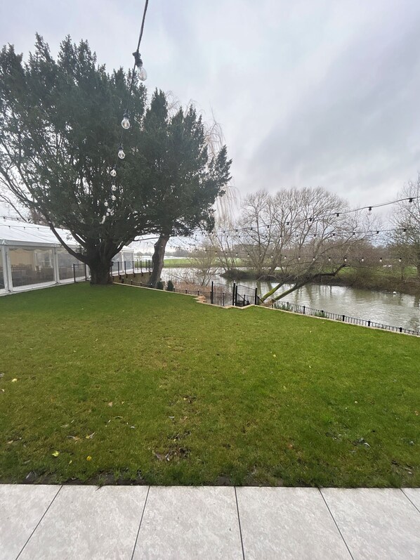 A grassy area with a large tree, a fence, and a body of water in the background. - The Mill Sharnbrook (Bedford)