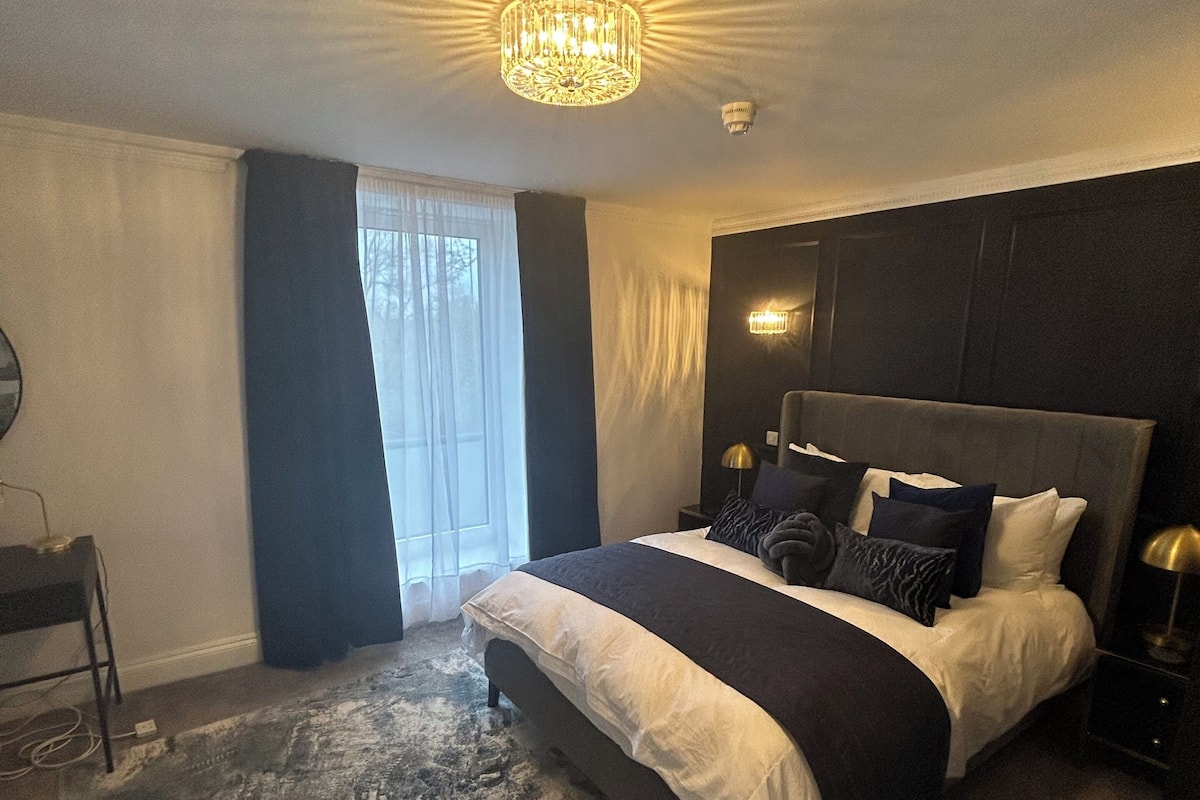A modern bedroom with a large bed, a chandelier, and a view of the outdoors.