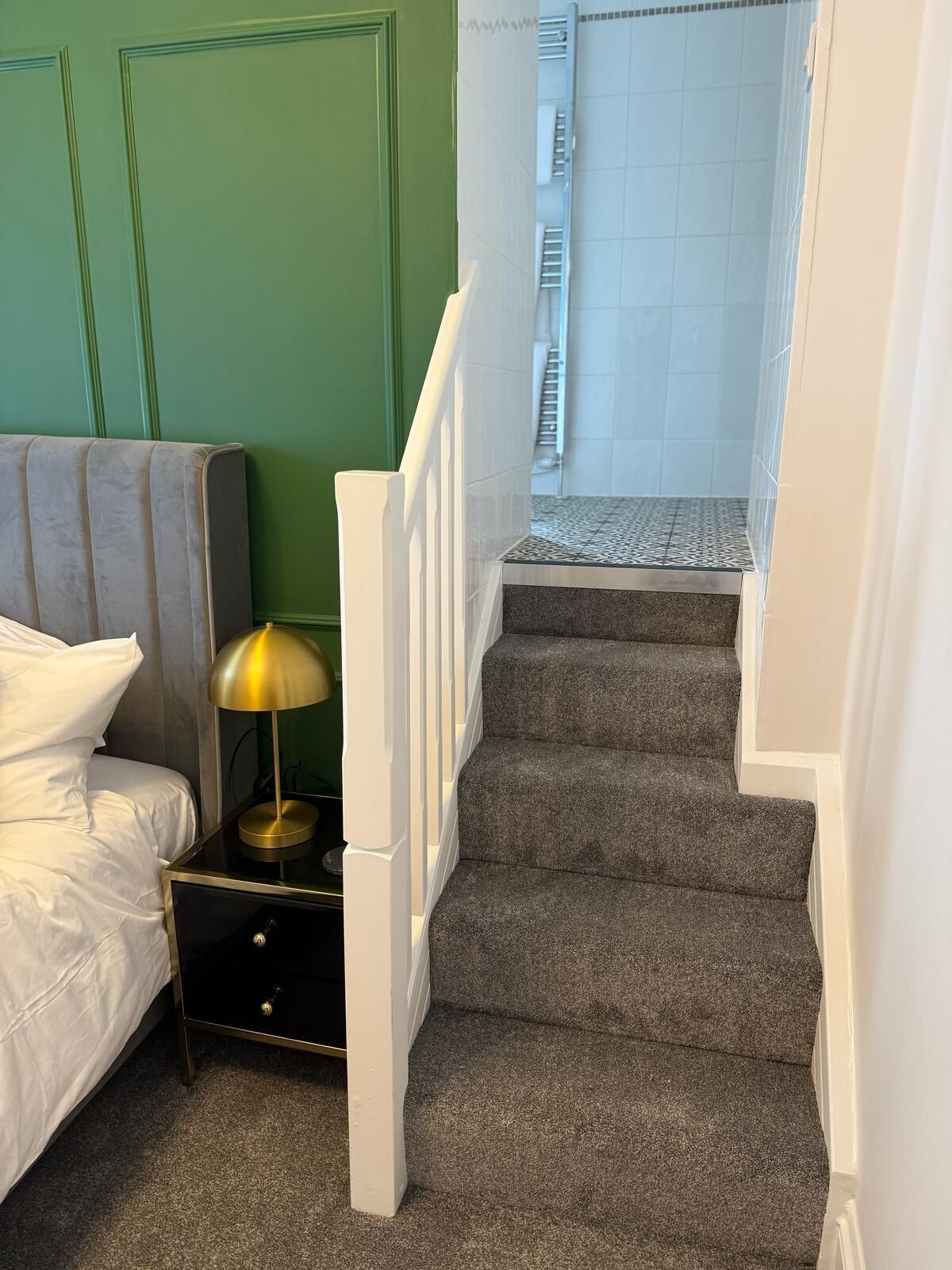Un dormitorio con cama, mesita de noche, lámpara y una escalera que lleva a un baño.