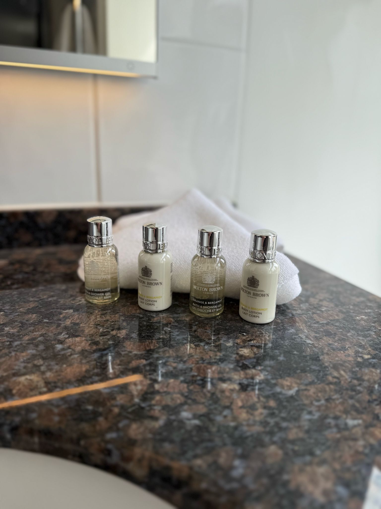 Four bottles of body lotion on a granite countertop in a bathroom.