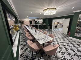 Una larga mesa de comedor con sillas rosadas, un candelabro y un suelo con estampado geométrico.
