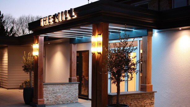 A hotel entrance with a covered patio, stone walls, and potted plants. - The Mill Sharnbrook (Bedford)