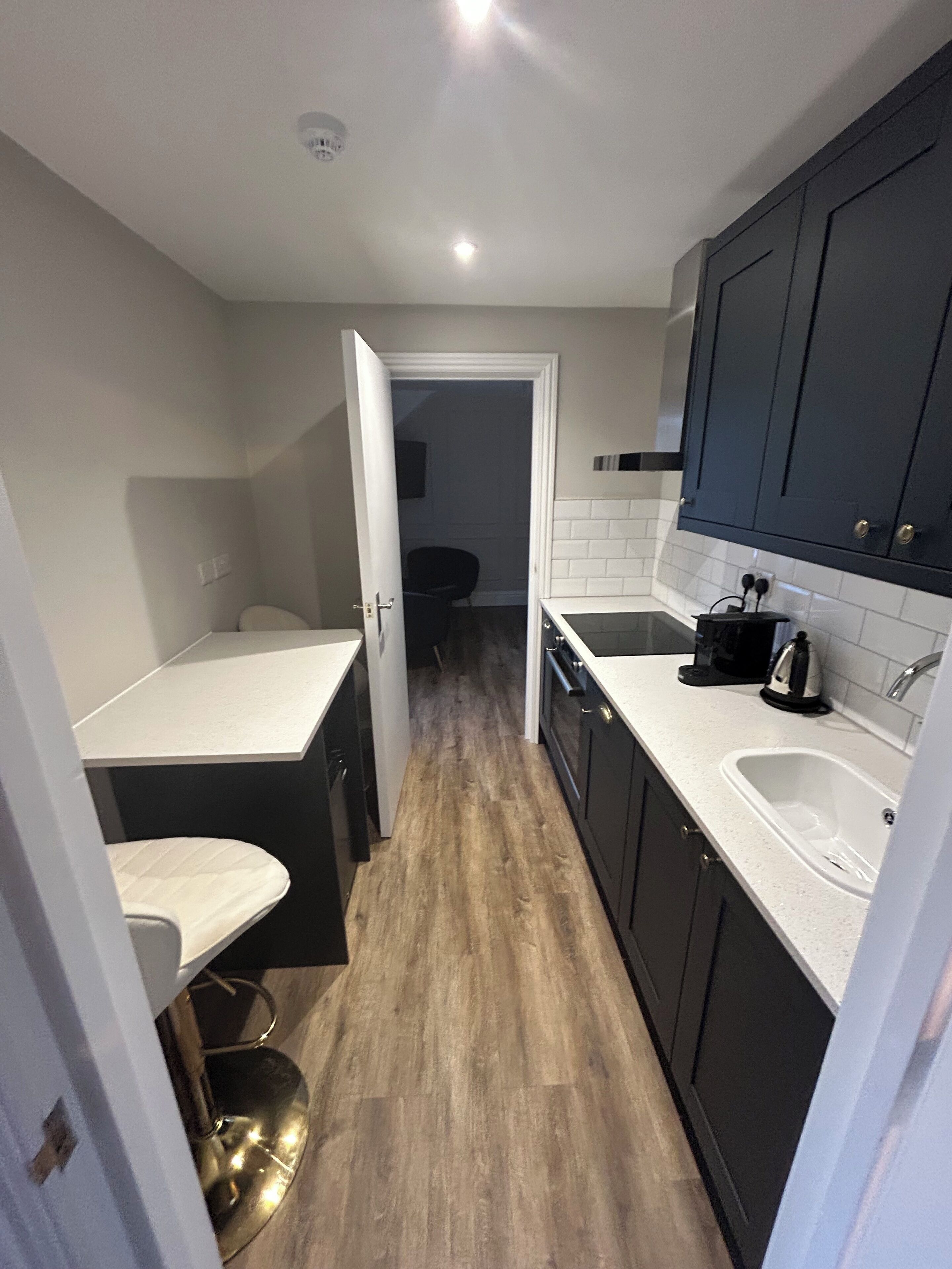 A compact kitchen with dark cabinets, a white countertop, and a wooden floor.