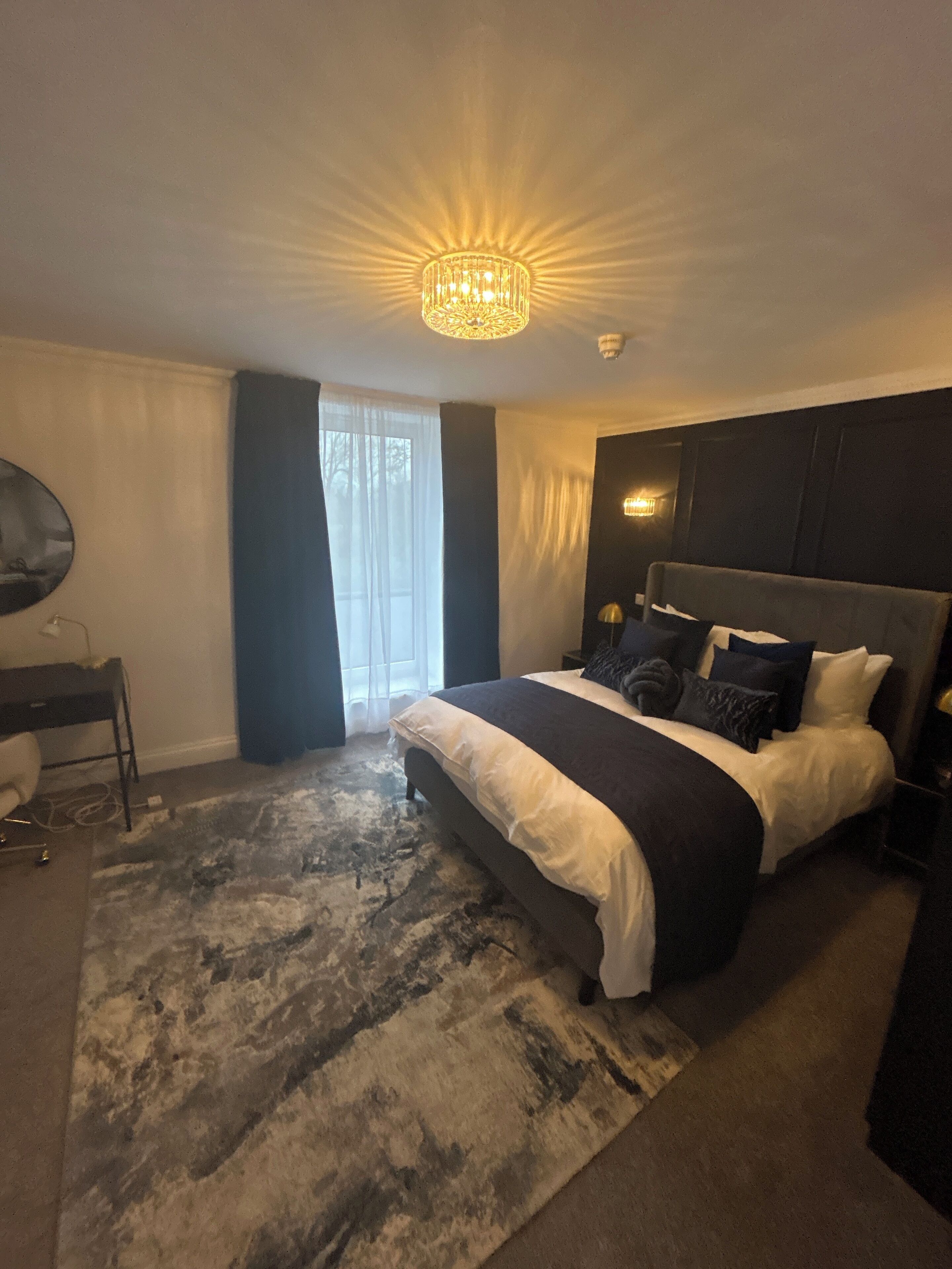 A modern bedroom with a large bed, a desk, and a chandelier.