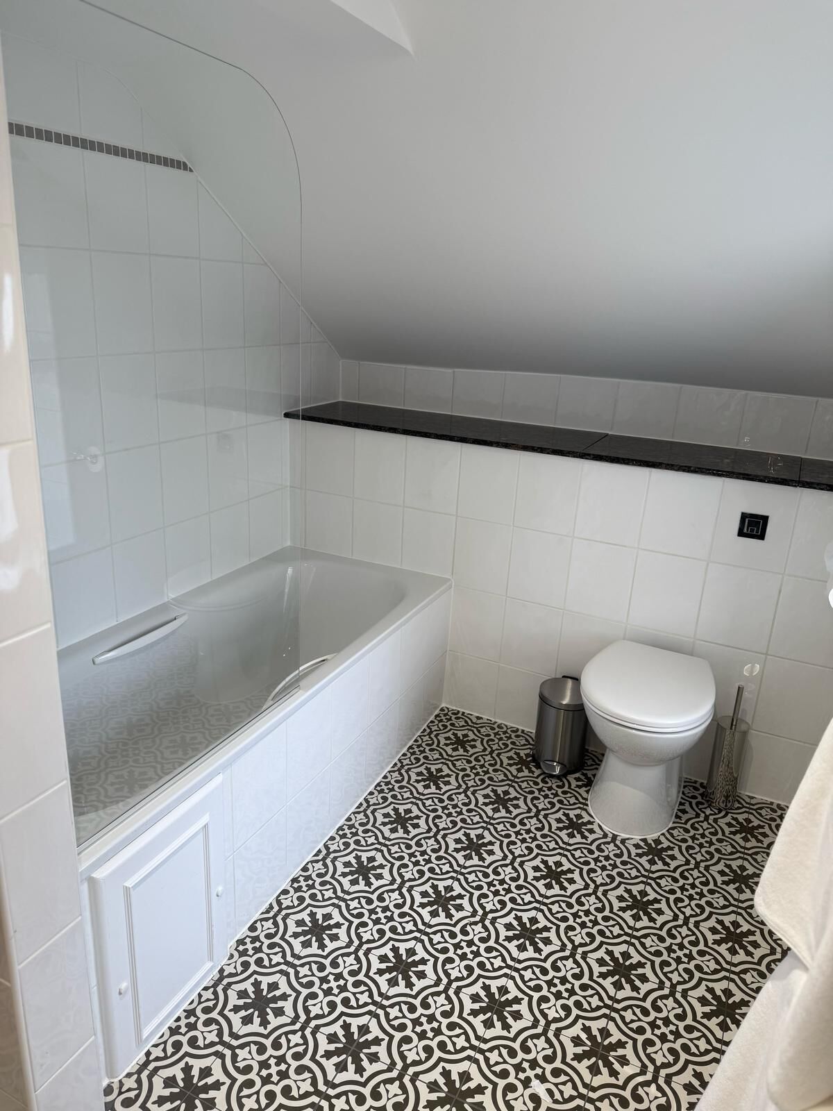 A bathroom with a bathtub, toilet, and patterned floor tiles.