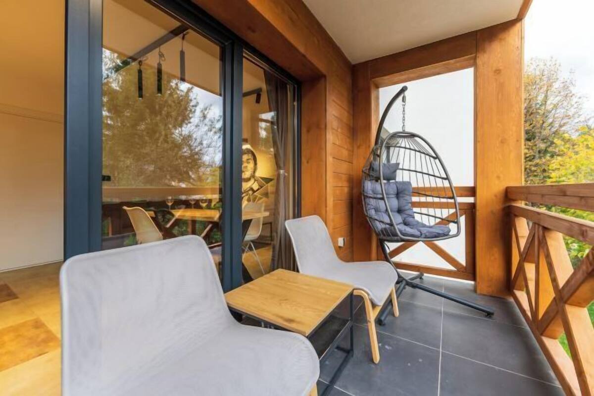 Un balcón con dos sillas y una hamaca colgante, barandilla de madera y vistas al exterior.