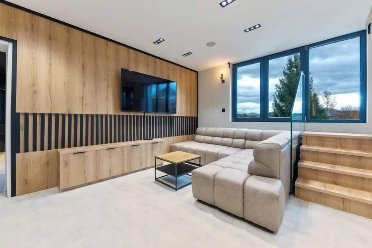 Una sala de estar moderna con un sofá modular, una mesa de centro y un televisor montado en una pared de madera.