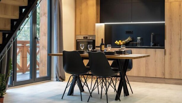 Une cuisine moderne avec un coin repas, comprenant un escalier en bois, de grandes fenêtres et un plan de travail noir.