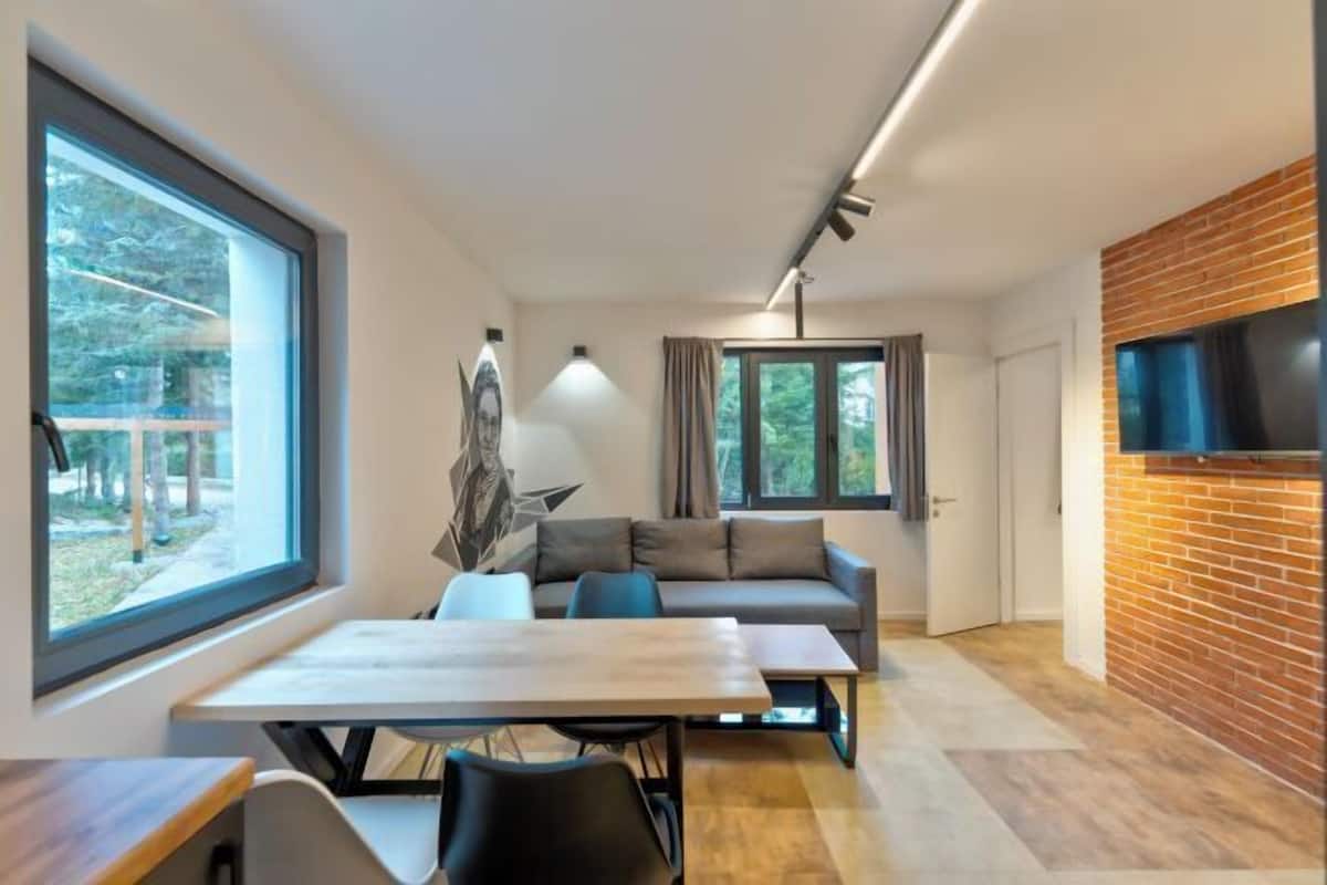 Una sala de estar moderna con comedor, ventanas grandes y una pared de ladrillo decorativa.