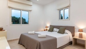 Un dormitorio con una cama grande, dos lámparas de noche y una ventana con vista a árboles.