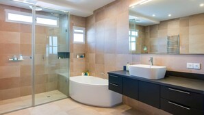 Un baño moderno con ducha envuelta en cristal, una bañera independiente y un tocador con un espejo grande.