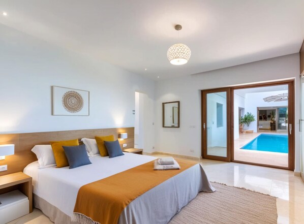 Un dormitorio moderno con una cama grande, una mesita de noche, un espejo en la pared y vista a una piscina al aire libre.