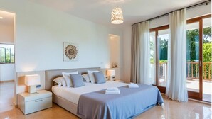 Un dormitorio moderno con una cama grande, mesitas de noche, un candelabro en el techo y vistas al exterior a través de una puerta corrediza de vidrio.