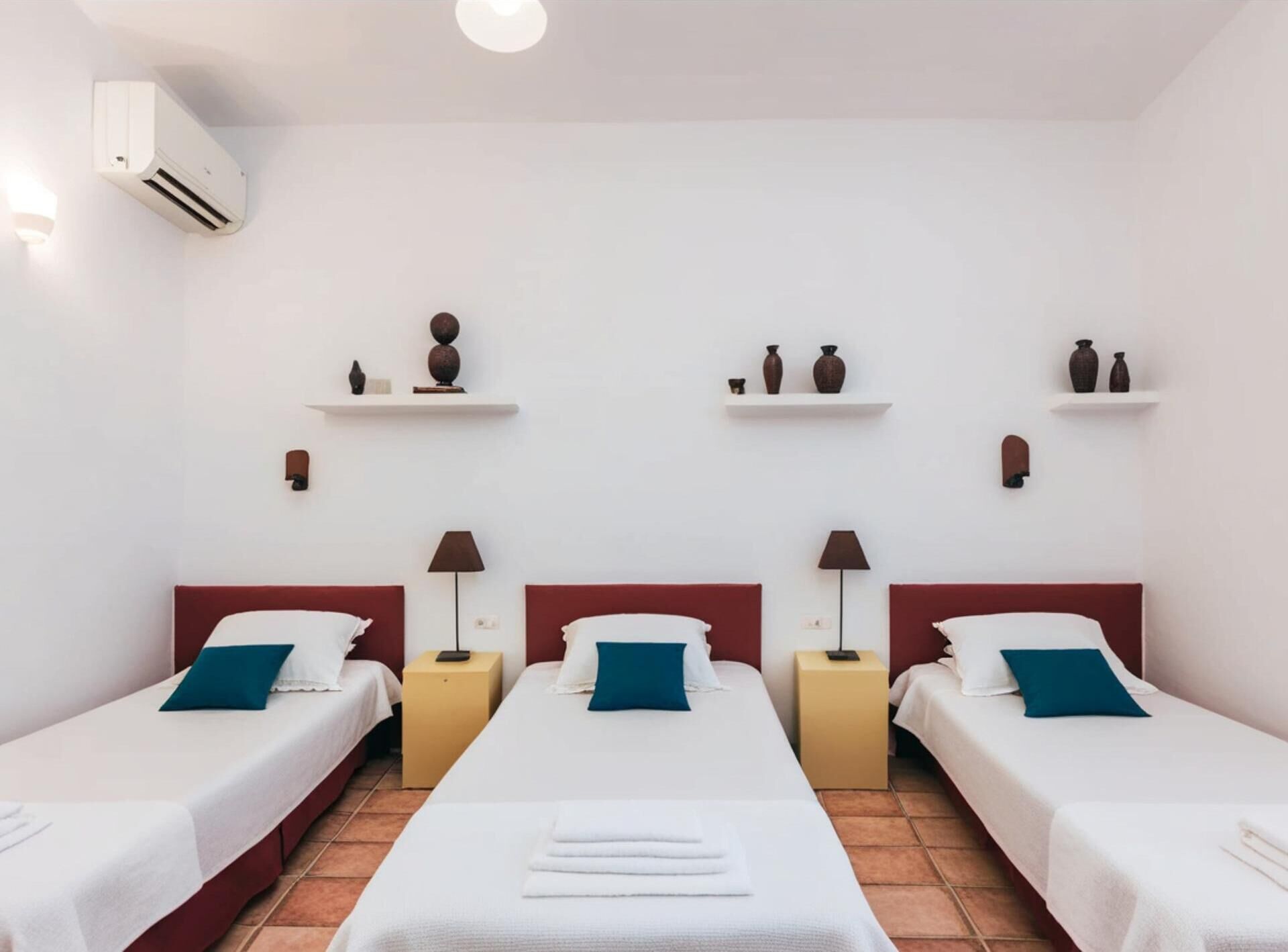 Ein Hotelzimmer mit drei Einzelbetten, einer Wandklimaanlage und dekorativen Regalen mit Vasen.