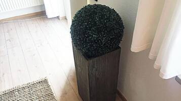 Um canto com piso de madeira, um cachepot de madeira escura com topo esférico e uma cortina branca.