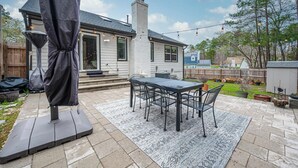 Un patio con una mesa y sillas, una sombrilla y una casa al fondo.