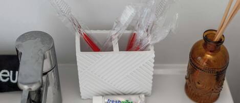 A bathroom sink with a toothbrush holder containing toothbrushes, a tube of freshmint toothpaste, and a decorative bottle.