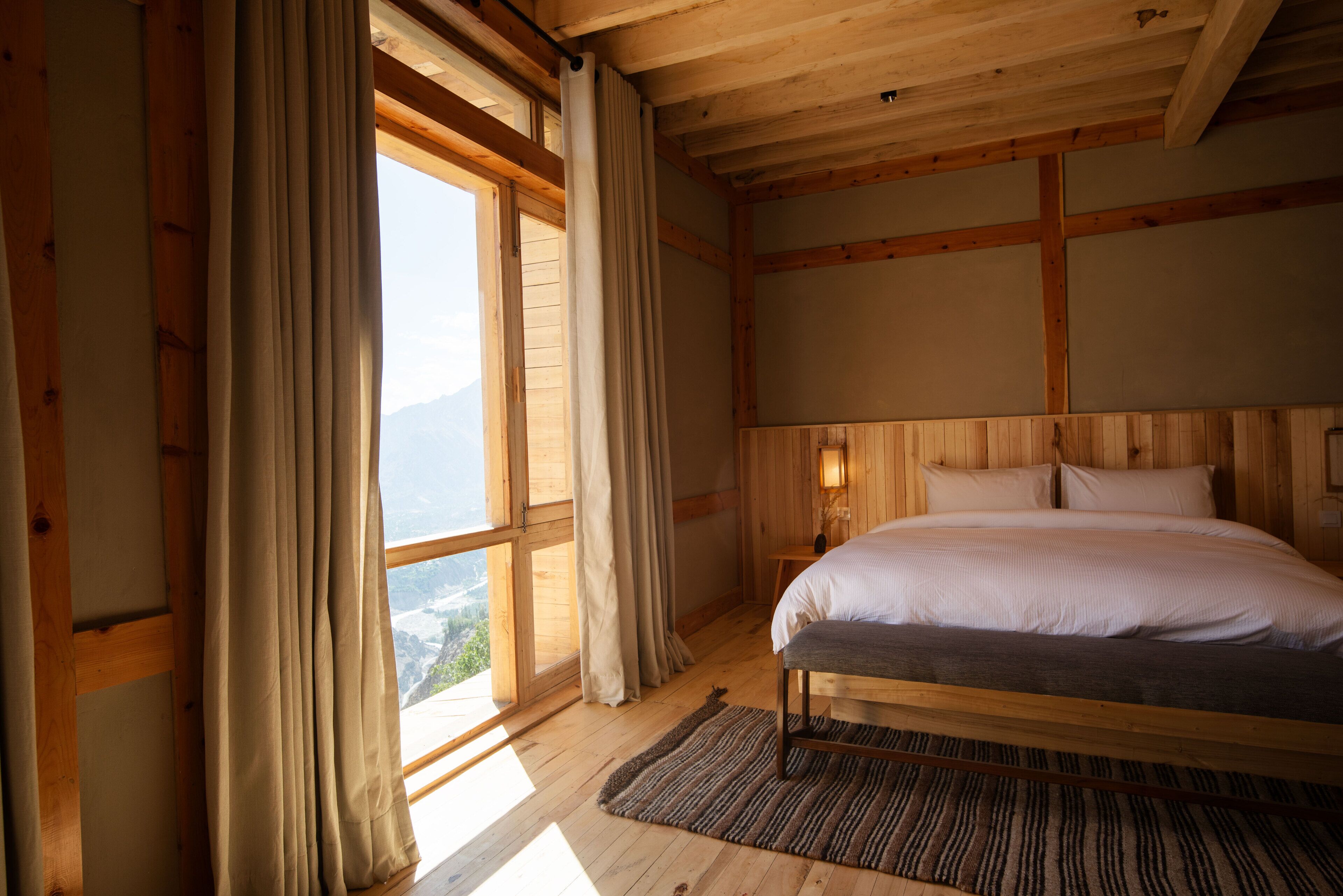 A wooden room with a bed, curtains, and a view of mountains.