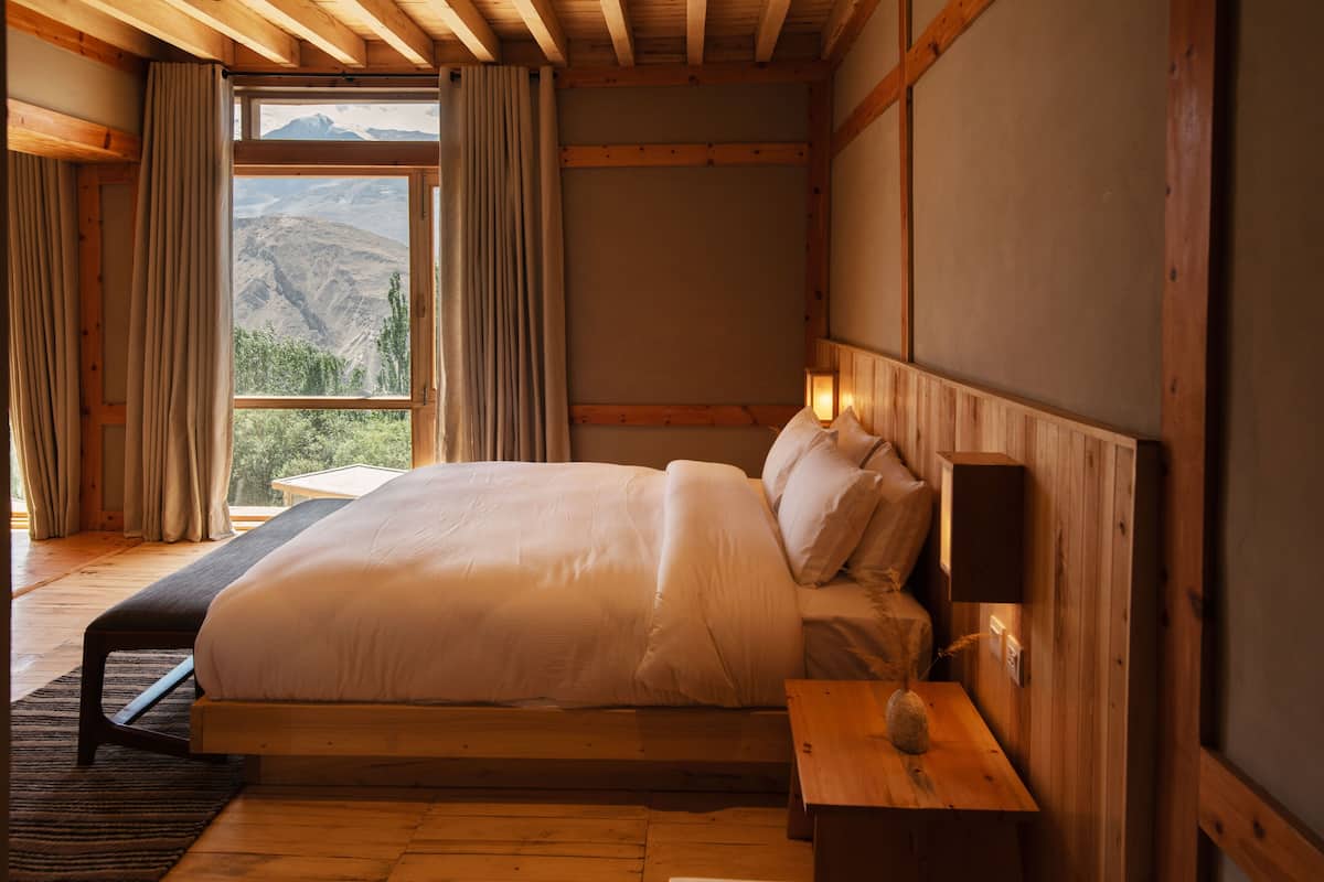 Une chambre avec un grand lit, des murs en bois, une table de chevet et une fenêtre avec des rideaux.