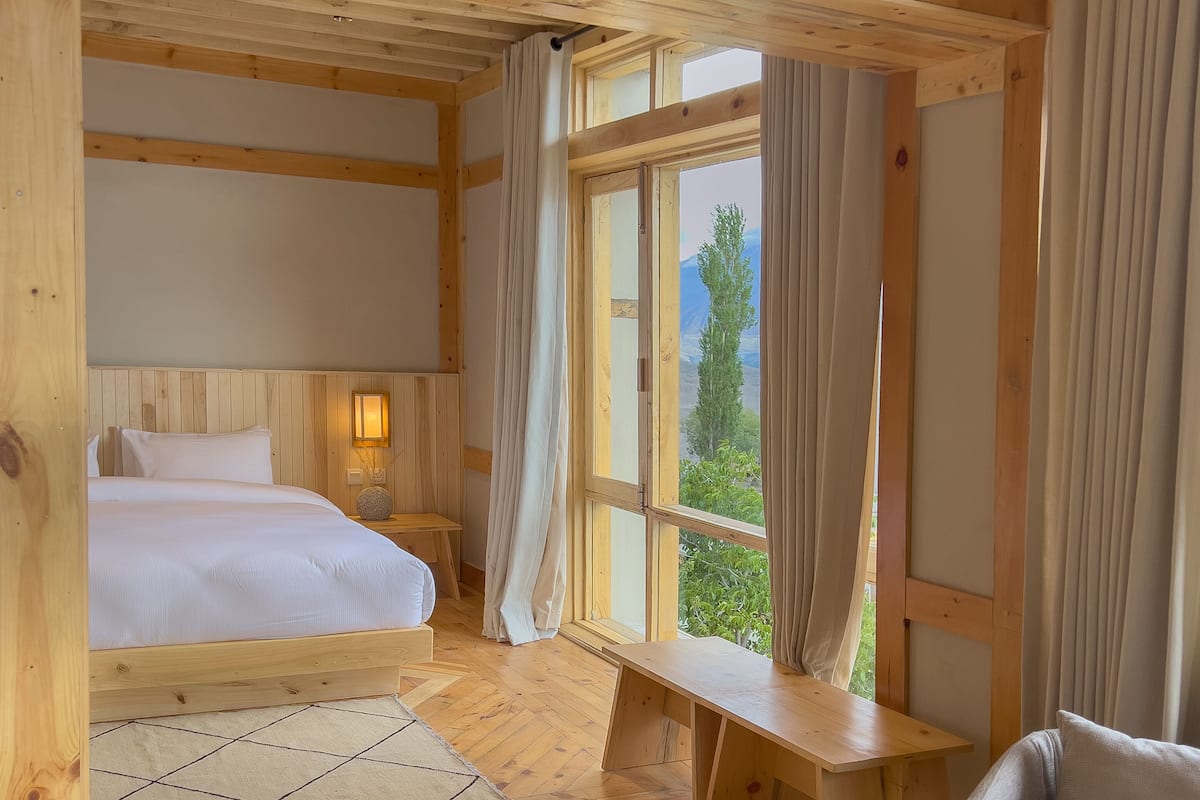 Une chambre dans une cabane en bois, avec deux lits, un banc et une vue sur la verdure.