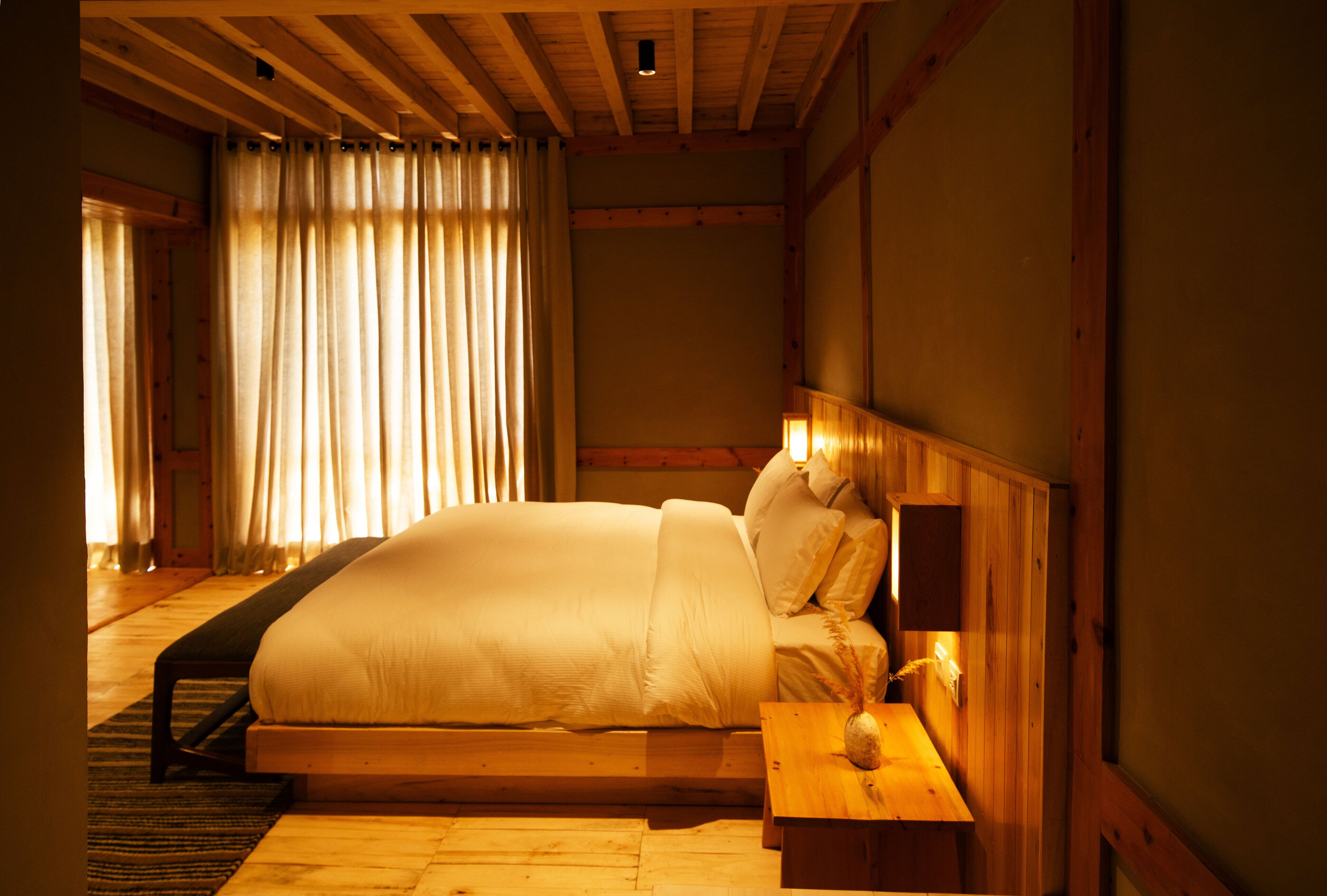 Un dormitorio con una cama de madera, una mesita de noche con lámpara y una ventana con cortinas.