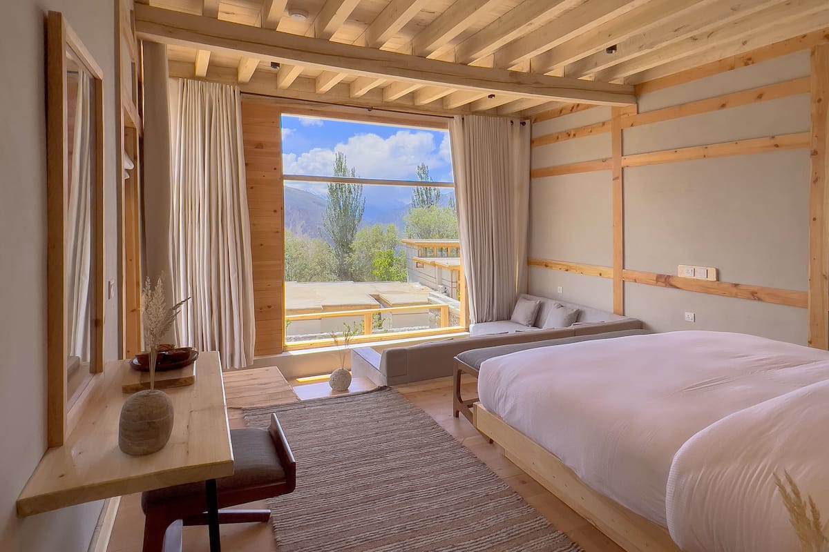 Une chambre avec un grand lit, un bureau en bois, une vue sur l’extérieur et une fenêtre avec des rideaux.