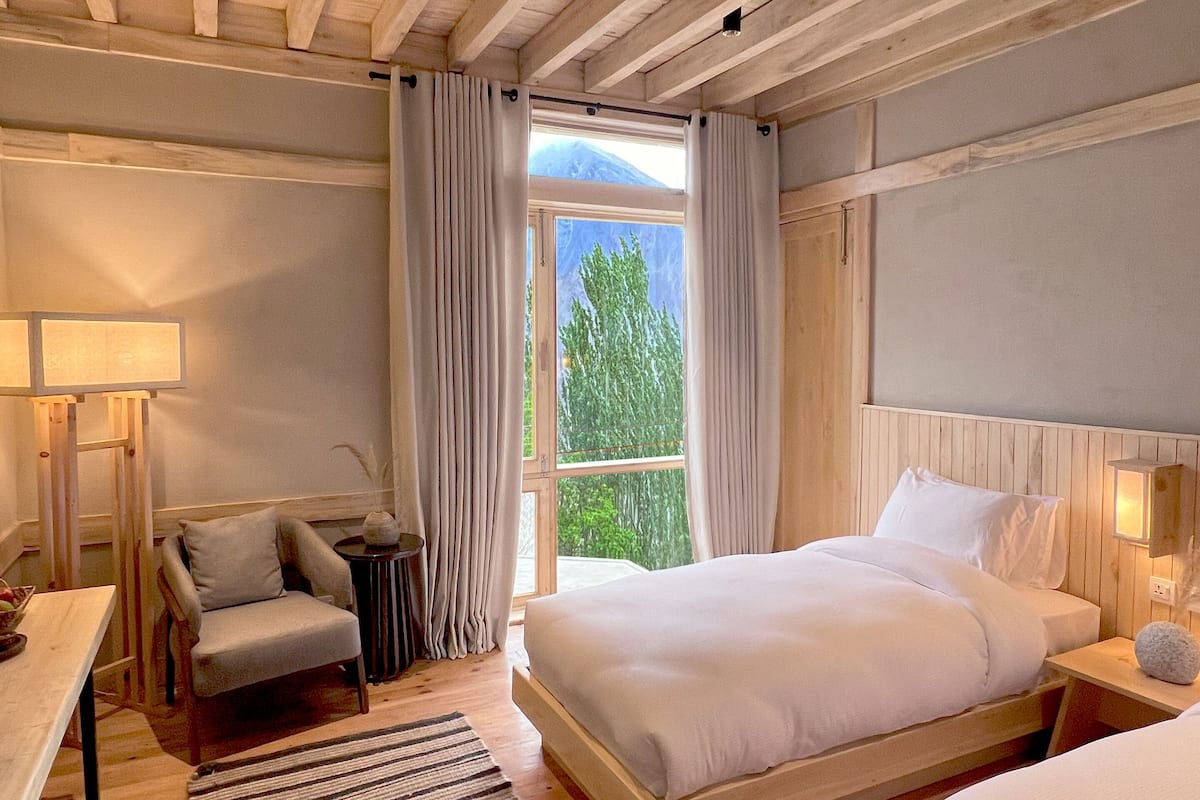 Une chambre à coucher avec un grand lit, une chaise, un bureau et une fenêtre avec des rideaux.