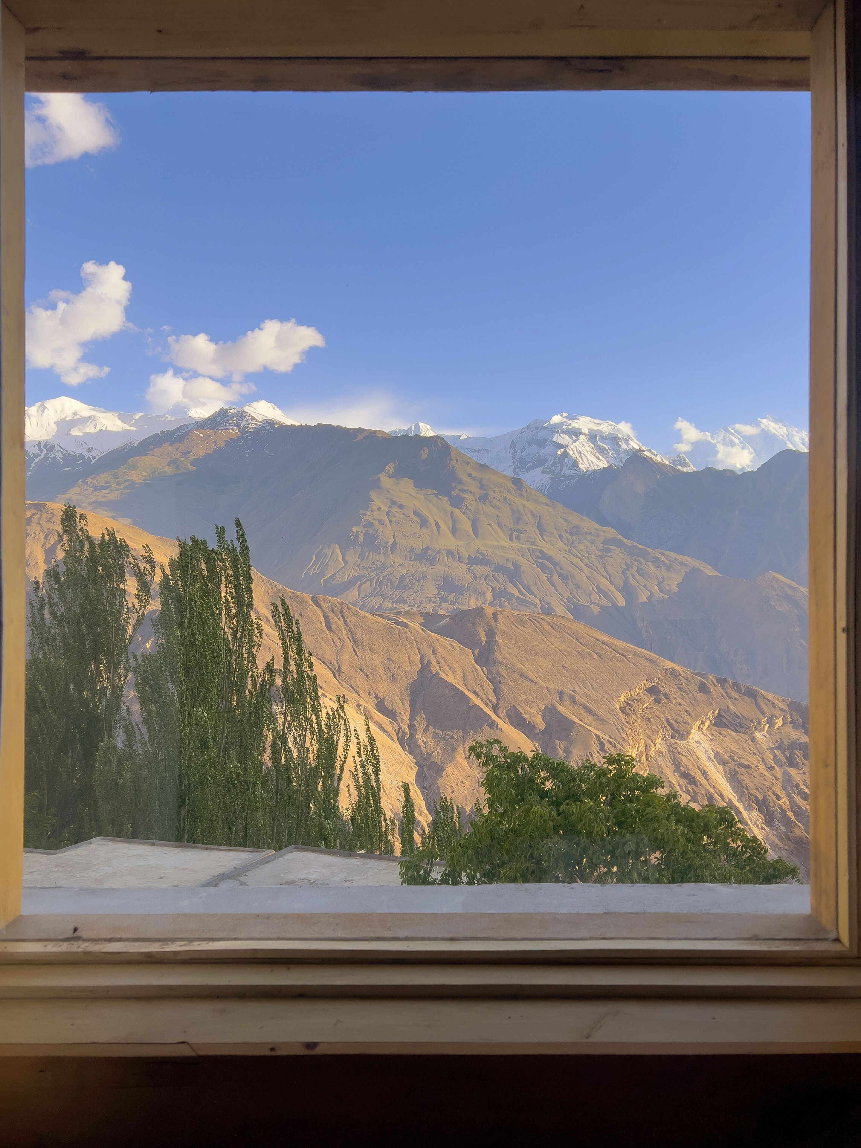 Un paysage de montagne vu à travers une fenêtre, avec des sommets enneigés et un ciel dégagé.