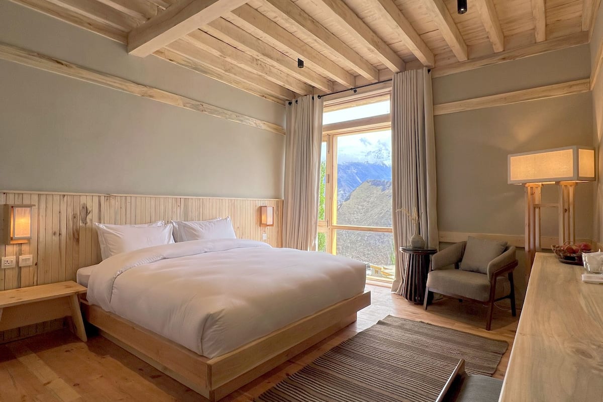 Une chambre spacieuse avec un grand lit, des poutres apparentes en bois au plafond, un bureau et une chaise.