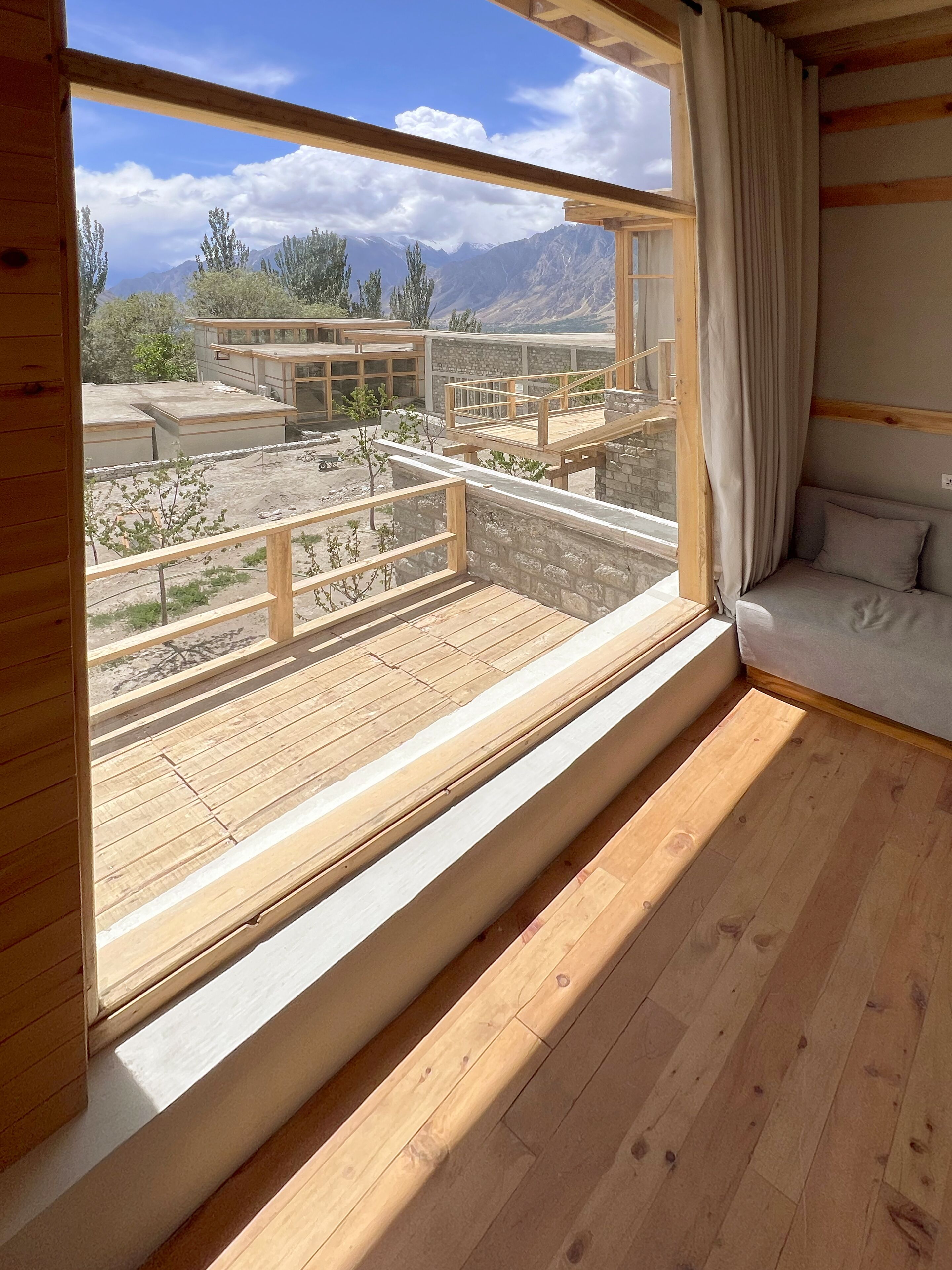 A room with a large window overlooking a mountainous landscape, wooden flooring, and a built-in bench with cushions.