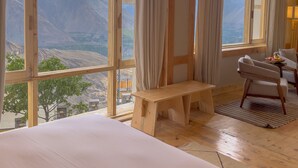 A room with large windows offering a mountain view, a wooden bench, and a small table with a lamp. - The Rihla Hunza - Managed By Luxus (Karimabad)