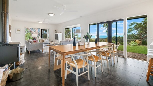 Un vaste espace de vie comprenant une table à manger en bois, des chaises blanches et une grande fenêtre donnant sur l’extérieur.