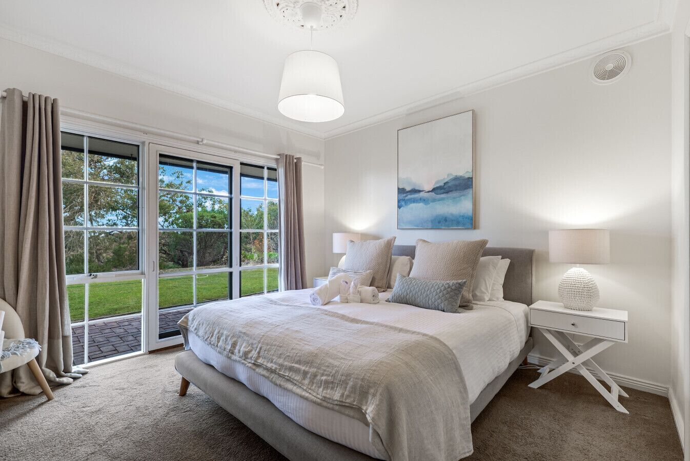 Een slaapkamer met een groot bed, een nachtkastje, een lamp, een schilderij en uitzicht op de natuur via een schuifdeur.