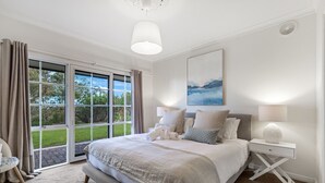 Une chambre à coucher avec un grand lit, une table de chevet, une lampe, un tableau et une vue sur l’extérieur grâce à une porte coulissante.