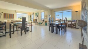 A spacious living area with a dining table, chairs, a sofa, and a coffee table. There are large windows providing natural light and a view of the city. - L'Artiste (Cannes)