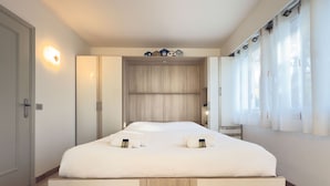 Een moderne hotelkamer met een groot bed, een inbouwkleerkast en uitzicht op de stad door grote ramen.