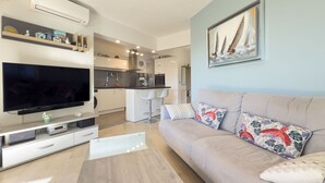 Een moderne woonkamer met een flatscreen televisie, een bank met patroon kussens en een keuken op de achtergrond.