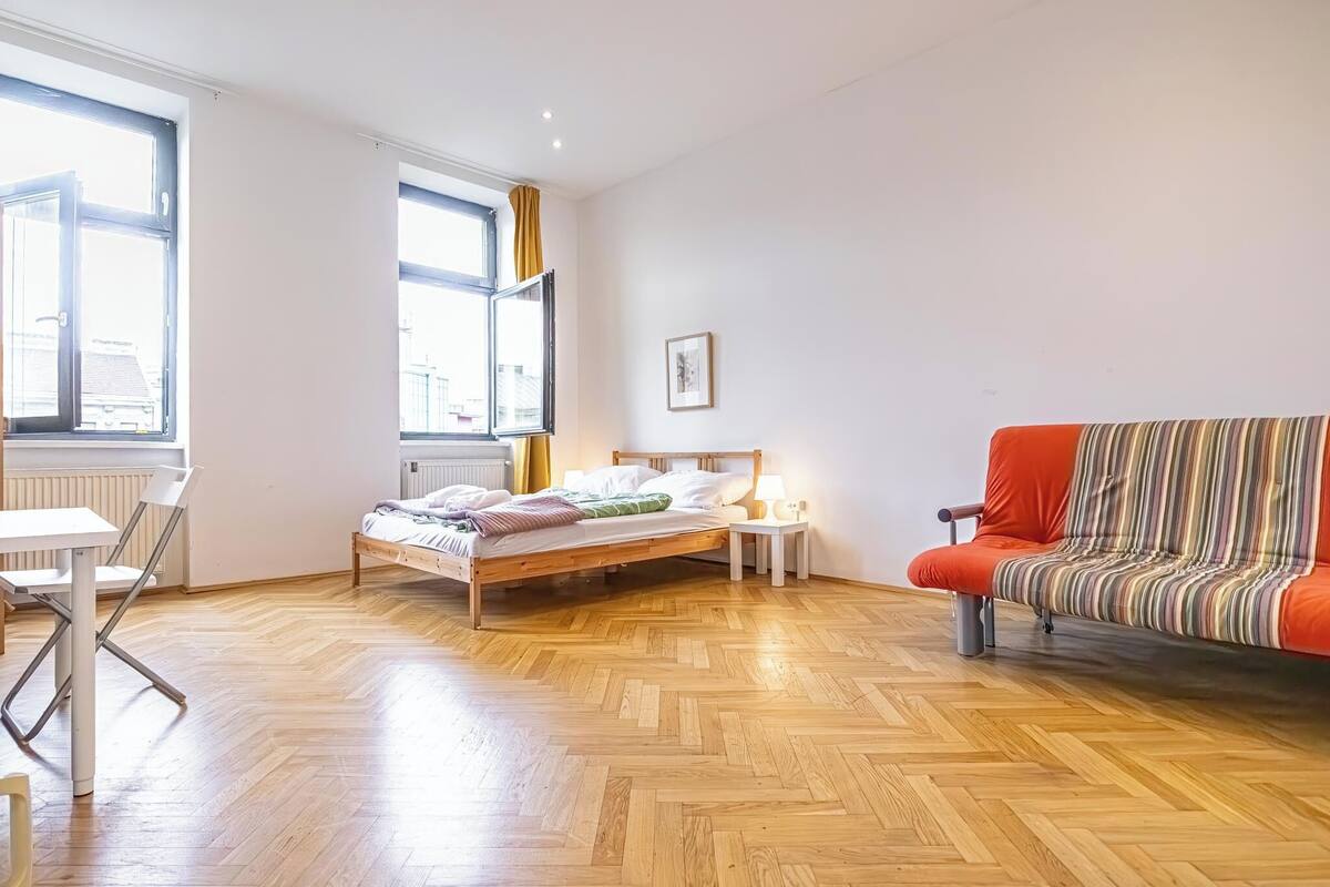 Une chambre à coucher avec un lit, une chaise, une petite table, un canapé et une fenêtre.