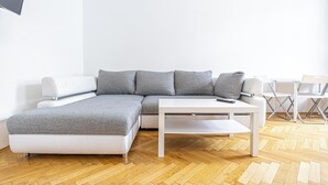Una sala de estar moderna con un sofá seccional gris, una mesa de centro blanca y un televisor montado en la pared.