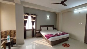 A hotel room with a bed, a nightstand, a table with a bottle, a window with curtains, and a ceiling fan. - DhamStay Hotel UK Palace Near Beach Puri (Puri)