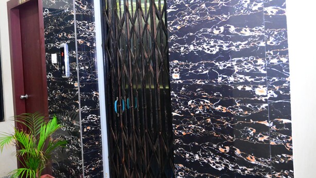 A modern entrance with a black marble wall, a metal gate, and a potted plant. - DhamStay Hotel UK Palace Near Beach Puri (Puri)
