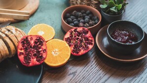 Una mesa con diversas frutas, una tetera y recipientes con mermelada.